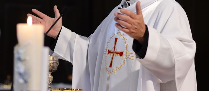 Ein Priester steht am Altar und spricht das Gabengebet über Wein und Brot.