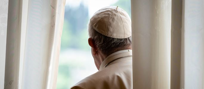 Papst Franziskus steht hinter einem Vorhang und guckt aus einem Fenster